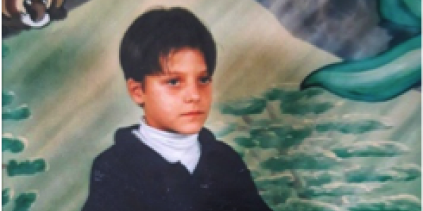 A picture of the author in 3rd grade. Shows a boy sitting in front of a painted background.